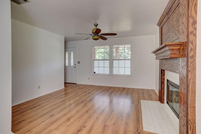 unfurnished living room with ceiling fan, a tile fireplace, visible vents, and light wood-style floors