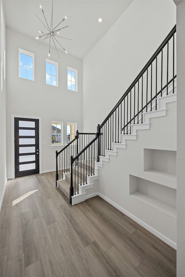 foyer entrance featuring a towering ceiling, hardwood / wood-style floors, and a notable chandelier