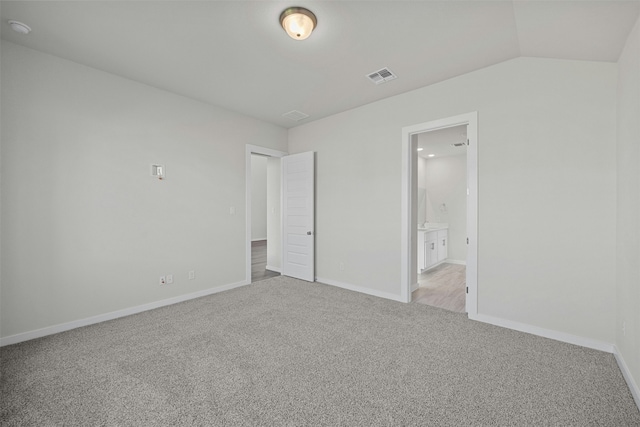 unfurnished bedroom featuring vaulted ceiling, connected bathroom, and light colored carpet