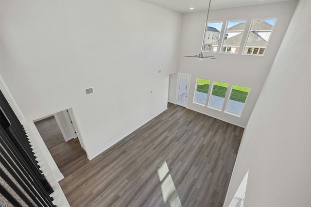 unfurnished living room with a towering ceiling, dark wood-type flooring, and ceiling fan