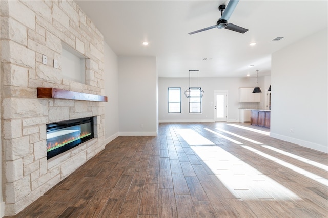 unfurnished living room featuring ceiling fan, a stone fireplace, and hardwood / wood-style flooring