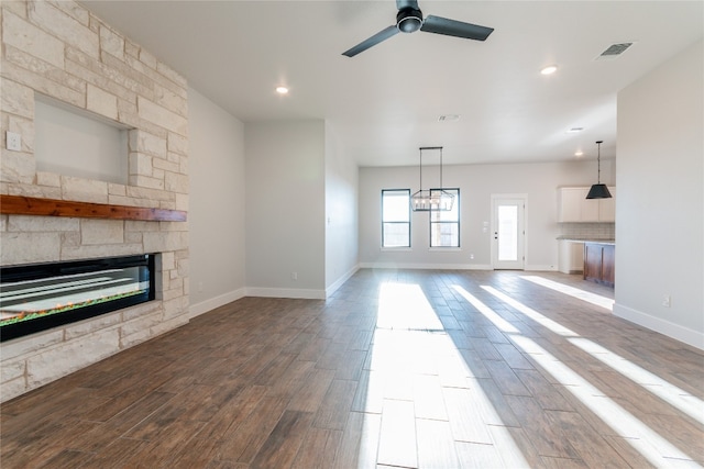 unfurnished living room featuring ceiling fan with notable chandelier, a stone fireplace, and dark wood-type flooring