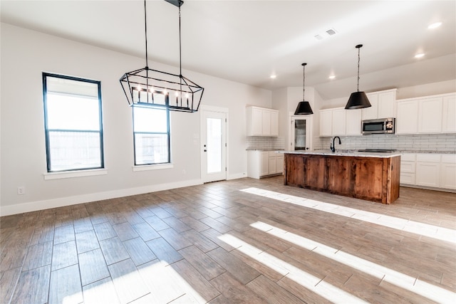 kitchen featuring a kitchen island with sink, white cabinets, pendant lighting, light hardwood / wood-style floors, and backsplash