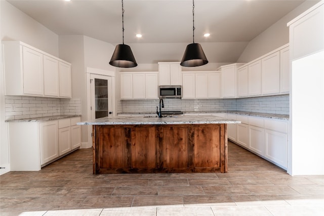 kitchen with backsplash, decorative light fixtures, a center island with sink, and white cabinetry