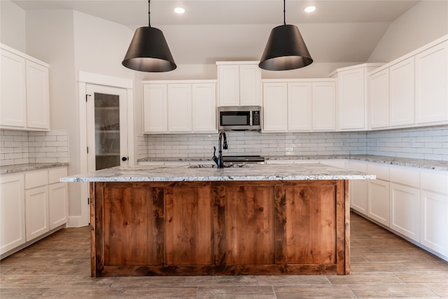 kitchen with sink, light hardwood / wood-style floors, a center island with sink, and decorative backsplash