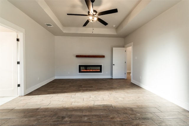 unfurnished living room featuring ceiling fan, light hardwood / wood-style flooring, and a tray ceiling