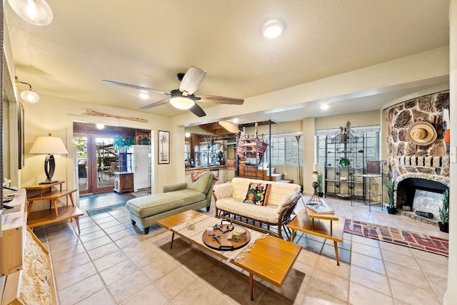 living room with a textured ceiling, ceiling fan, light tile patterned floors, and a stone fireplace