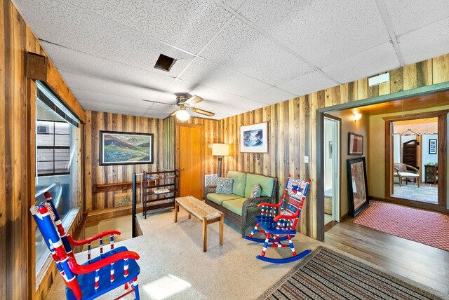 living room with a drop ceiling, wood walls, ceiling fan, and hardwood / wood-style flooring