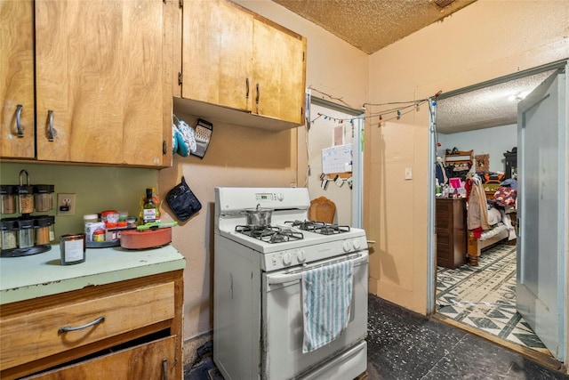 kitchen featuring a textured ceiling, white range with gas stovetop, and dark tile patterned floors