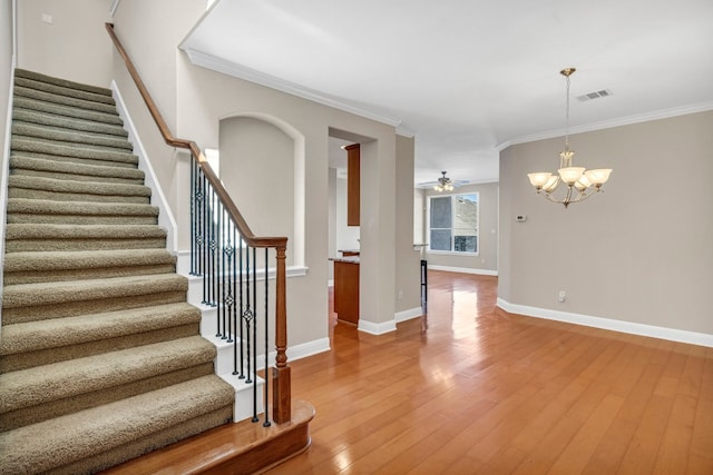 staircase with wood-type flooring, ceiling fan with notable chandelier, and ornamental molding