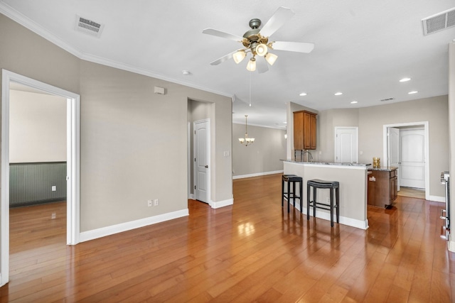 kitchen with a breakfast bar, ceiling fan with notable chandelier, pendant lighting, a center island, and hardwood / wood-style floors