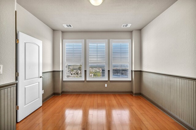 spare room with light wood-type flooring, a textured ceiling, and plenty of natural light