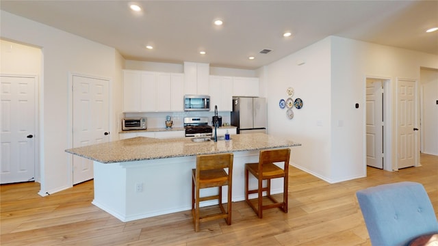 kitchen featuring light hardwood / wood-style flooring, white cabinets, light stone countertops, a center island with sink, and stainless steel appliances