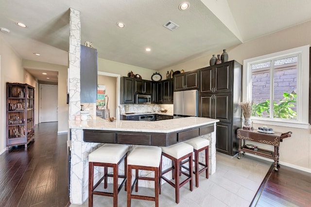 kitchen featuring appliances with stainless steel finishes, tasteful backsplash, a kitchen bar, vaulted ceiling, and kitchen peninsula