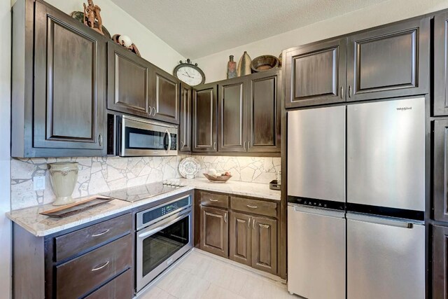 kitchen featuring stainless steel appliances, light stone countertops, and dark brown cabinets