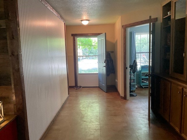 hallway with a textured ceiling, light tile patterned floors, and a healthy amount of sunlight