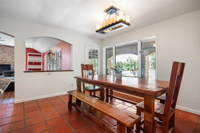 dining space featuring a notable chandelier, vaulted ceiling, and a brick fireplace