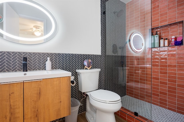 bathroom with tiled shower, toilet, tile walls, vanity, and ceiling fan