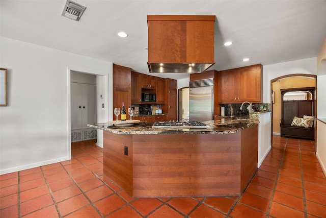 kitchen with dark stone countertops, tile patterned flooring, stainless steel appliances, and kitchen peninsula