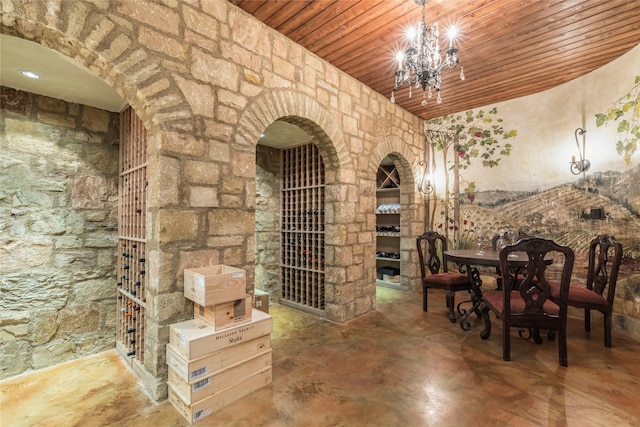 wine area featuring concrete flooring, a chandelier, and wooden ceiling