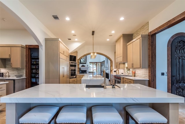 kitchen with a breakfast bar area, tasteful backsplash, a large island with sink, and light brown cabinetry