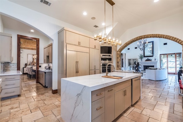 kitchen featuring pendant lighting, light stone countertops, a center island with sink, backsplash, and a chandelier