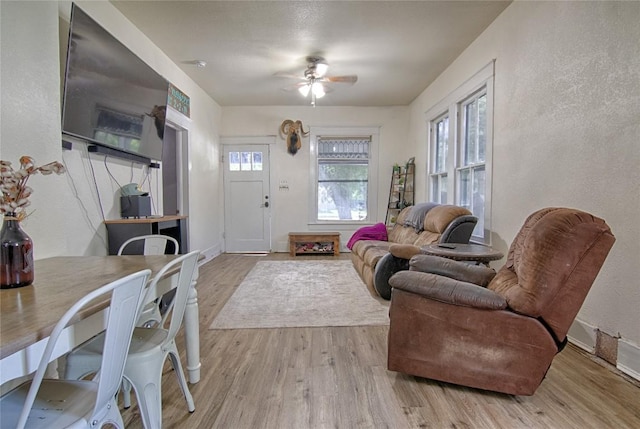 interior space featuring light wood-type flooring, a textured wall, baseboards, and ceiling fan