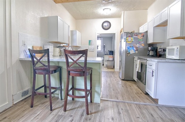 kitchen featuring light wood finished floors, appliances with stainless steel finishes, a breakfast bar, light countertops, and white cabinetry