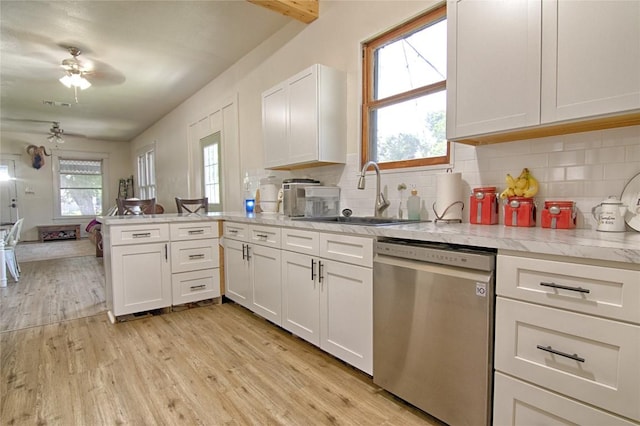 kitchen with a peninsula, stainless steel dishwasher, a sink, and white cabinetry