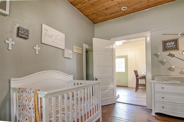 bedroom with a nursery area, wooden ceiling, and dark wood finished floors