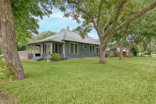 back of property featuring metal roof, a lawn, a chimney, and fence