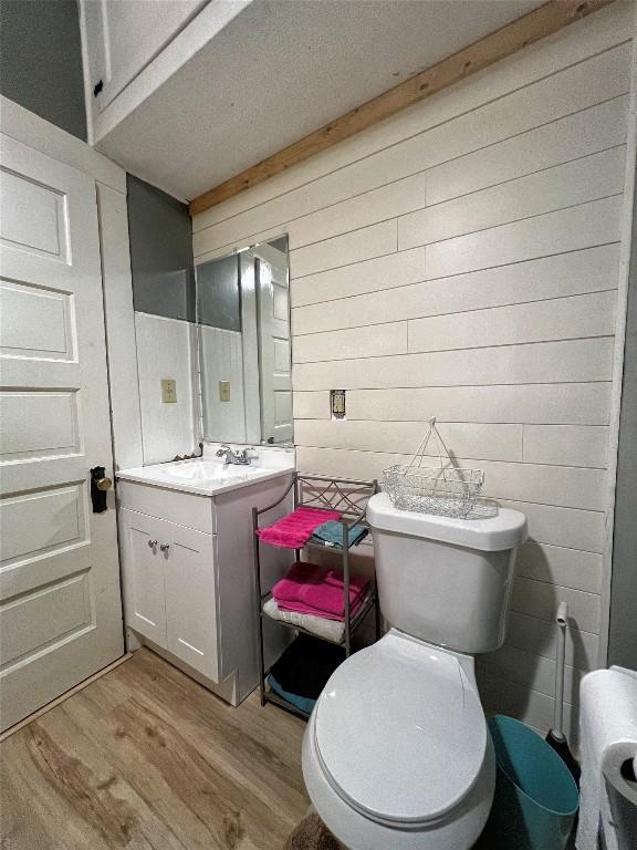 bathroom featuring toilet, wood walls, wood finished floors, and vanity