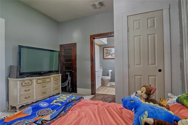 bedroom with light wood finished floors, connected bathroom, visible vents, and baseboards