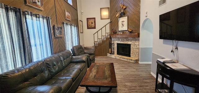 living room with dark wood-type flooring, a stone fireplace, wood walls, and a high ceiling