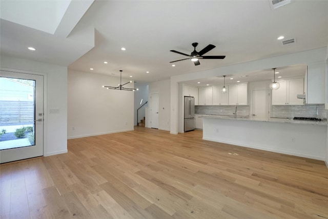 unfurnished living room with light wood-type flooring, sink, and ceiling fan with notable chandelier