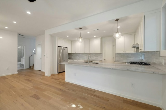 kitchen with appliances with stainless steel finishes, kitchen peninsula, decorative light fixtures, light wood-type flooring, and sink