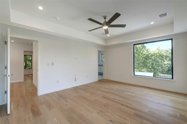 spare room featuring light wood-type flooring, ceiling fan, and a raised ceiling