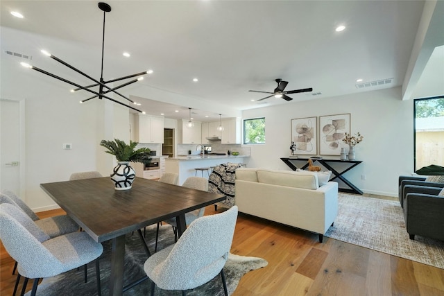 dining area with ceiling fan with notable chandelier, sink, and light hardwood / wood-style floors