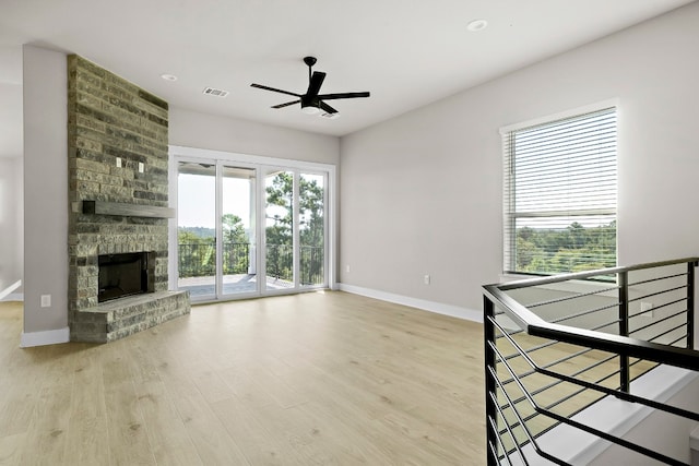 unfurnished living room featuring ceiling fan, plenty of natural light, a fireplace, and light wood-type flooring