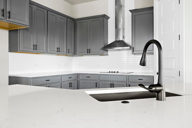 kitchen featuring wall chimney range hood, decorative backsplash, gray cabinets, and sink