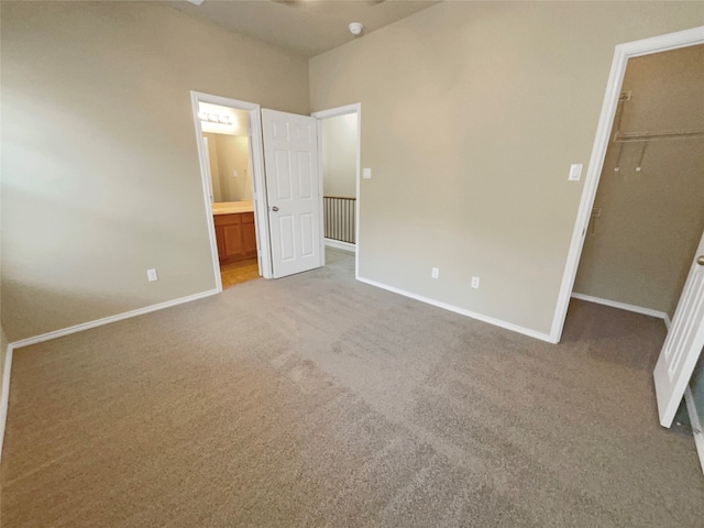 unfurnished bedroom featuring a spacious closet, ensuite bathroom, light carpet, and a closet