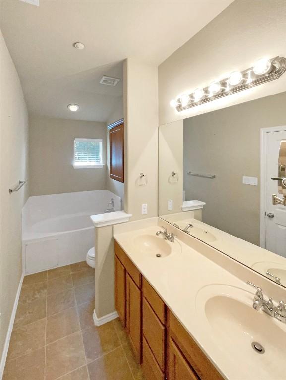 bathroom featuring dual bowl vanity, tile patterned floors, a washtub, and toilet