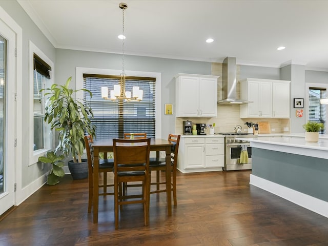 kitchen with hanging light fixtures, wall chimney exhaust hood, decorative backsplash, high end stove, and white cabinetry