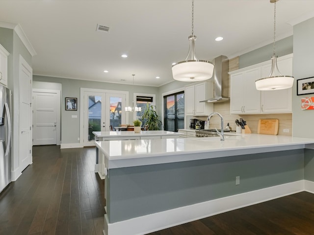 kitchen featuring backsplash, french doors, white cabinets, wall chimney range hood, and hanging light fixtures