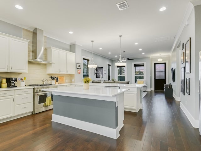 kitchen featuring kitchen peninsula, appliances with stainless steel finishes, wall chimney range hood, white cabinets, and a kitchen island