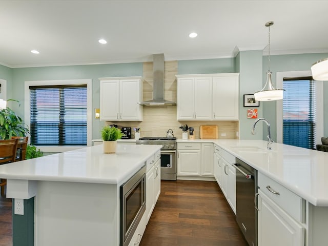 kitchen featuring sink, wall chimney range hood, a kitchen island, white cabinets, and appliances with stainless steel finishes