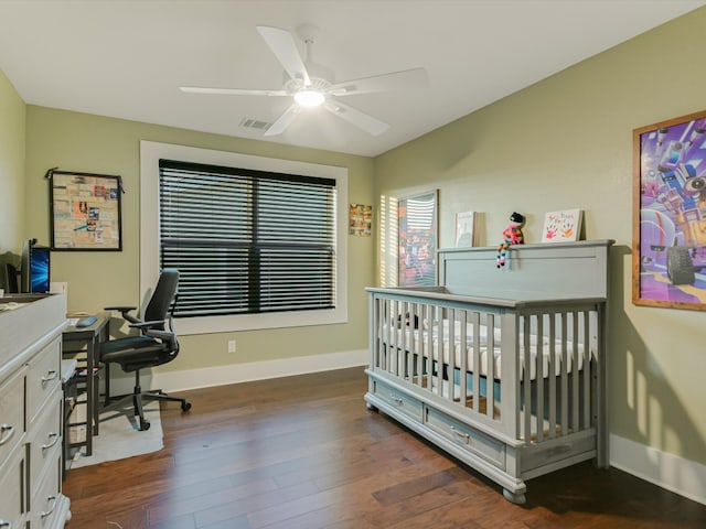 bedroom with ceiling fan, a crib, and dark wood-type flooring