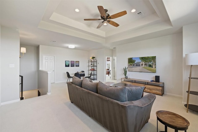 carpeted living room with ceiling fan and a tray ceiling