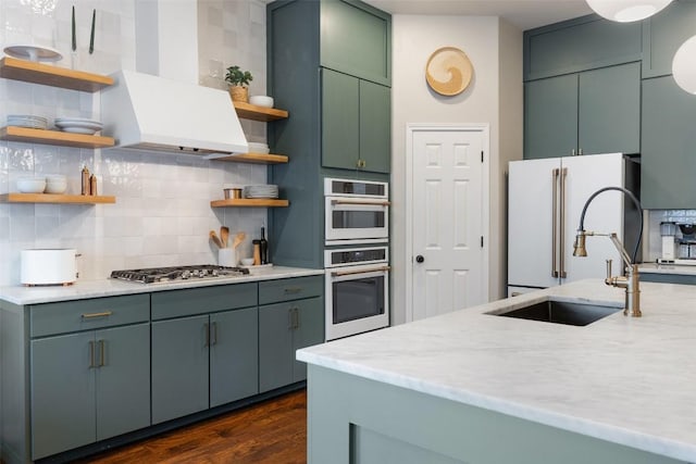 kitchen featuring sink, double wall oven, stainless steel gas stovetop, decorative backsplash, and wall chimney range hood