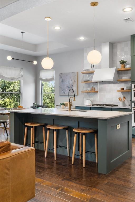 kitchen with an island with sink, sink, wall chimney range hood, and decorative light fixtures